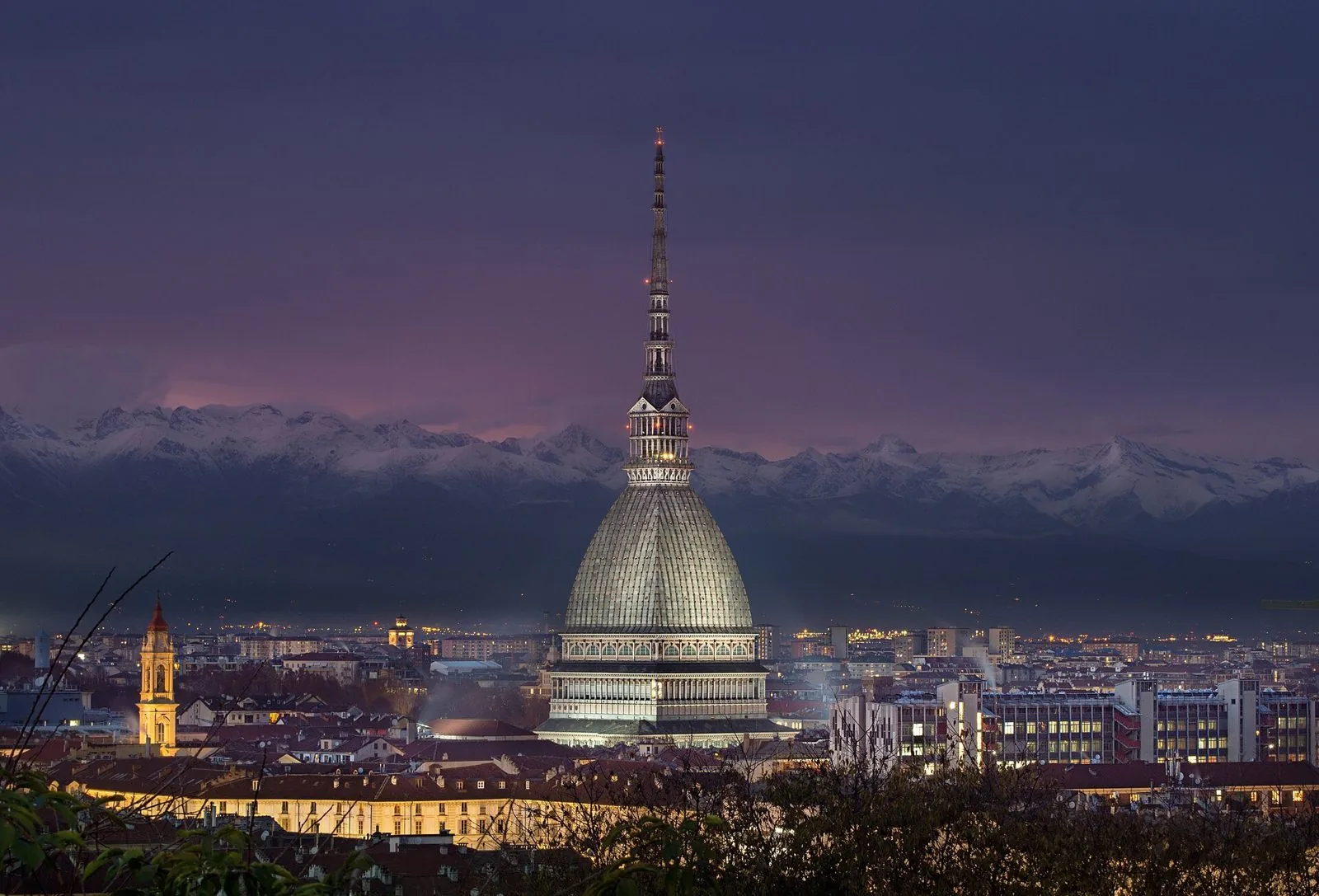 La Mole Antonelliana illuminata al crepuscolo con le Alpi innevate sullo sfondo